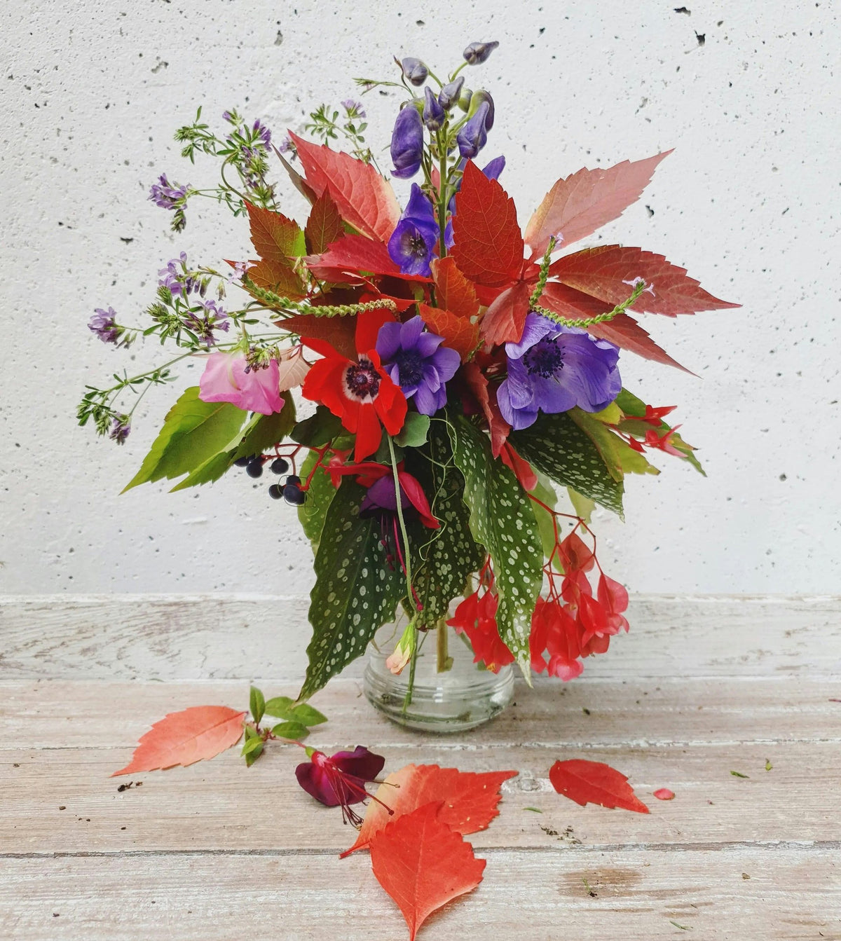 Autumn leaves, anemones and monkshood in a glass vase on a wooden table