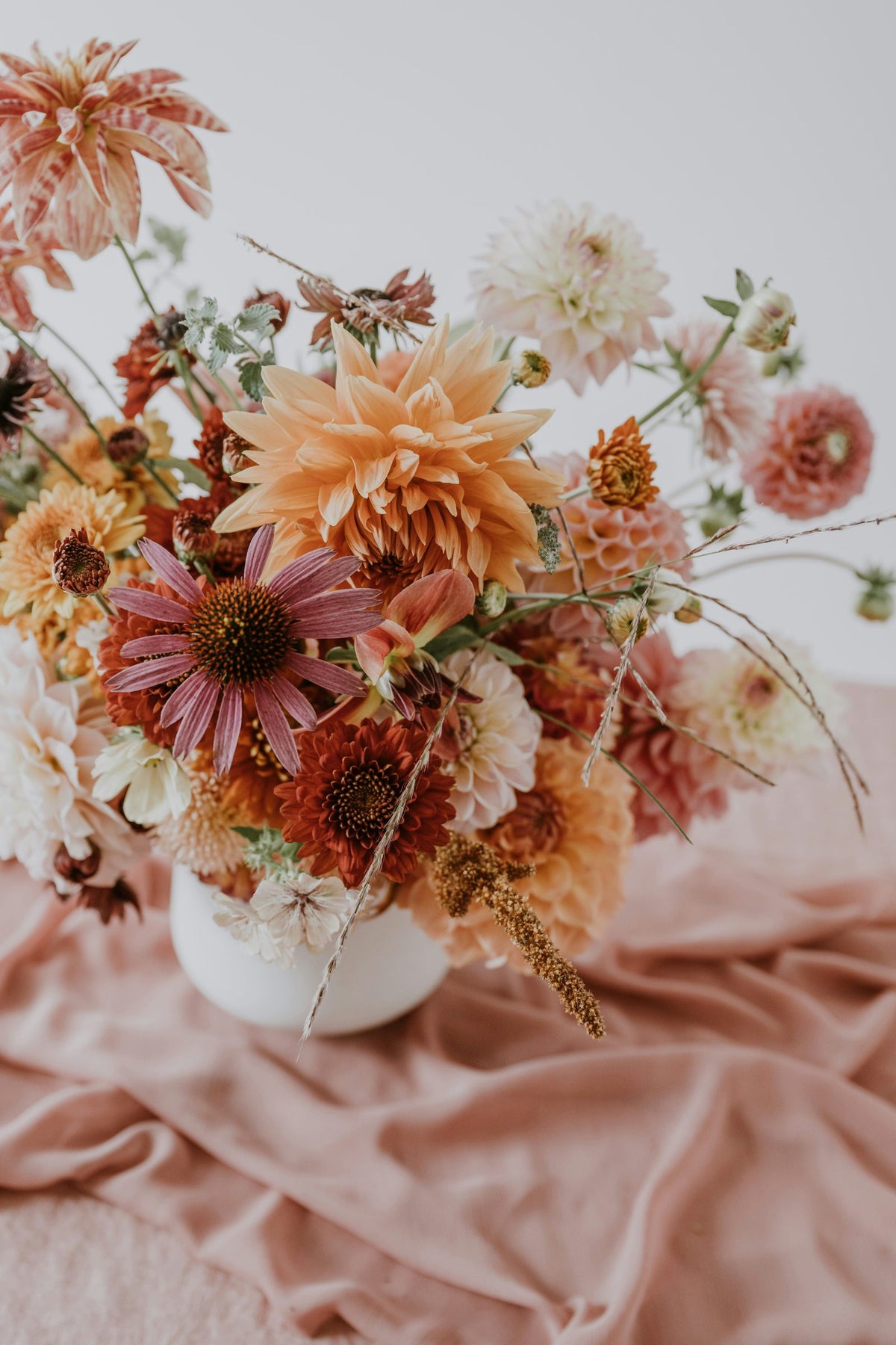Dahlias, cosmos and echinacea arranged in a white vase on a blush cloth