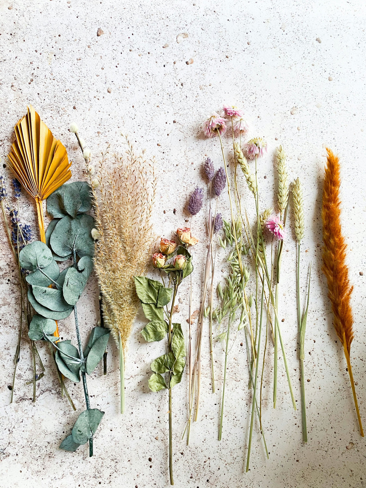 Dried palm, eucalyptus, grasses and rosebuds laid out on stone