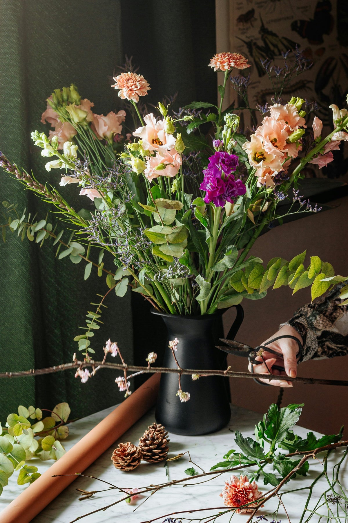 Florist arranging seasonal stems in a black jug in the studio