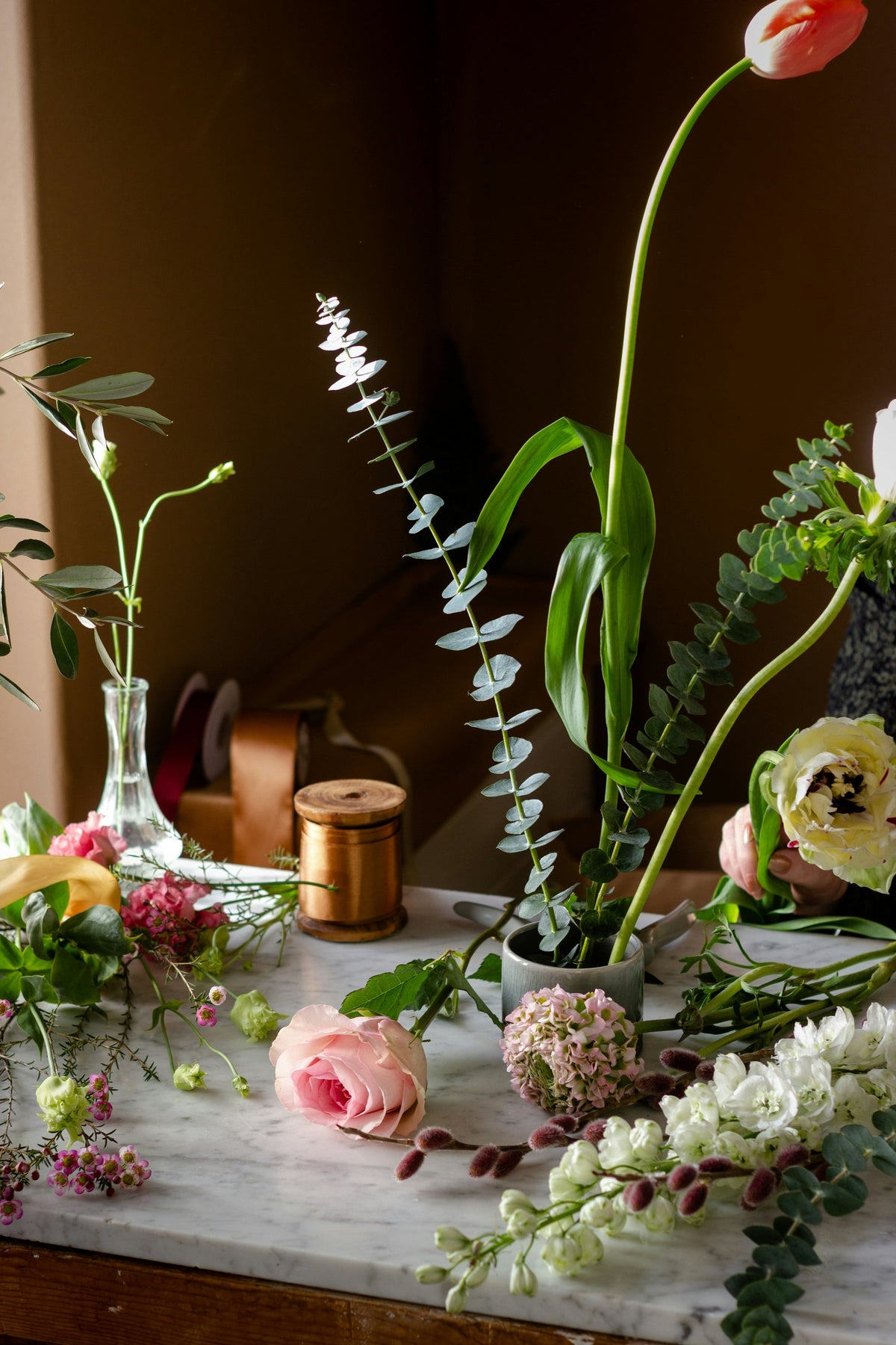 Florist bench with tulips, ranunculus, eucalyptus and a spool of ribbon