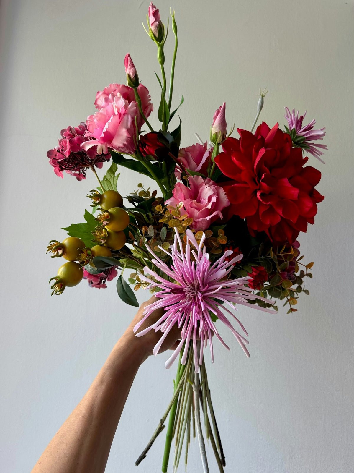 Hand holding up a hand-tied bouquet of pink and red flowers
