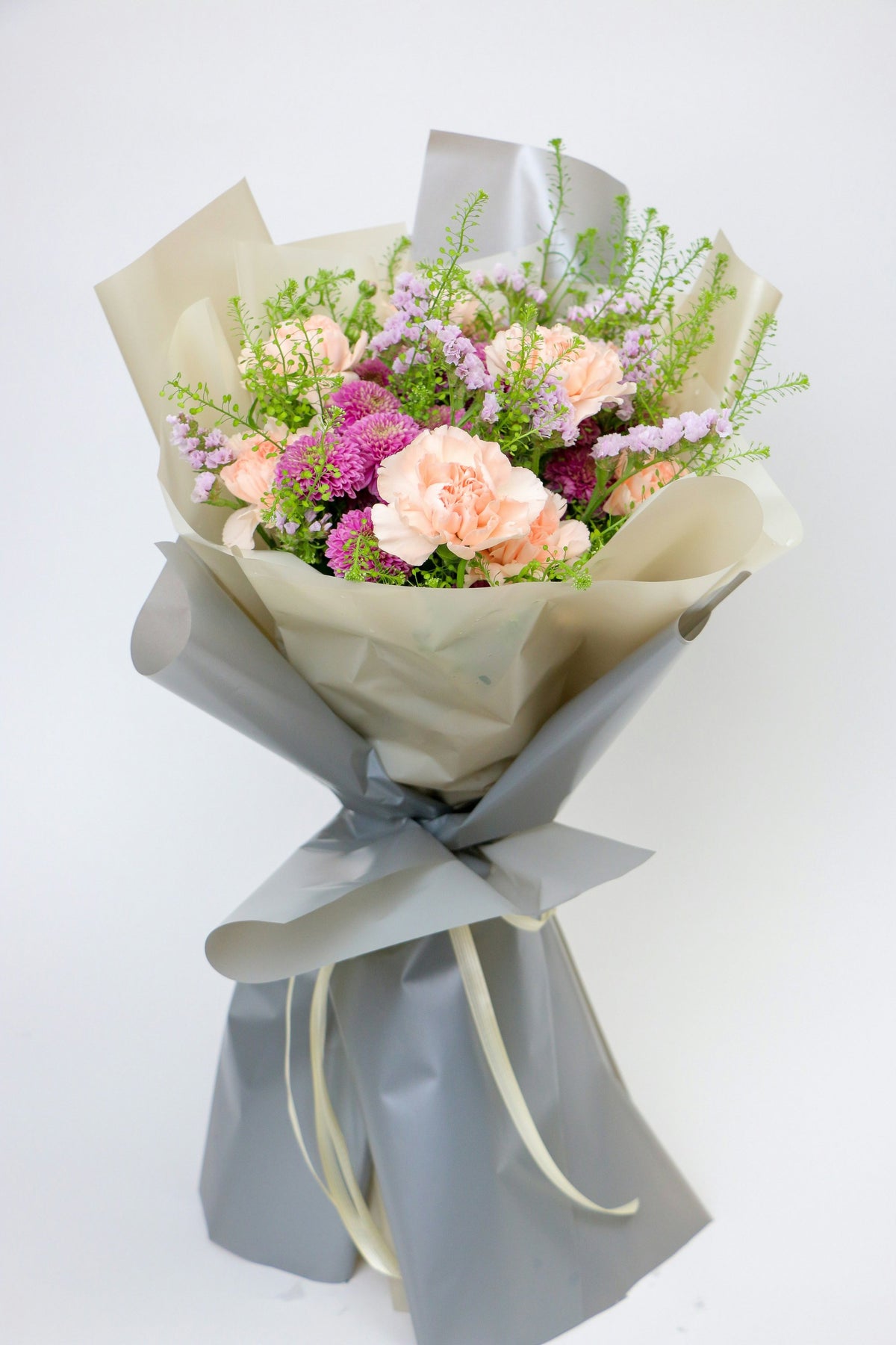 Pastel bouquet of peach carnations and pink blooms, wrapped in cream and grey paper