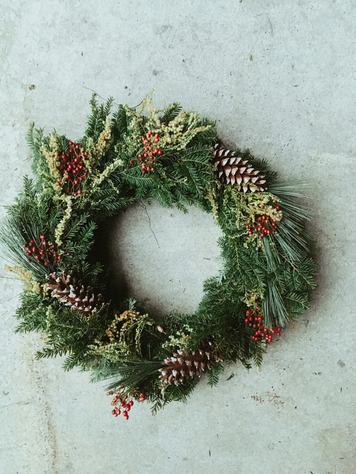 Pine wreath with pine cones and red berries on concrete