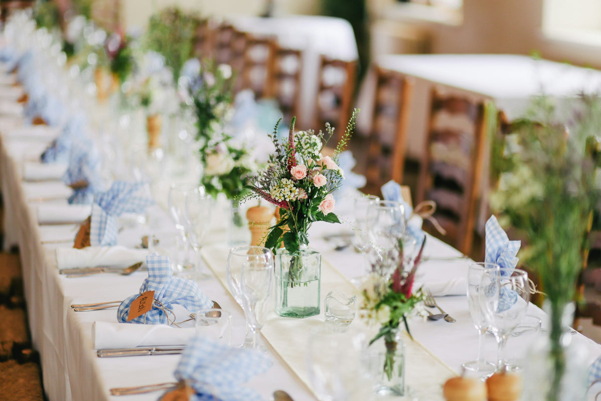 Long wedding table with posies in glass bottles and gingham napkins