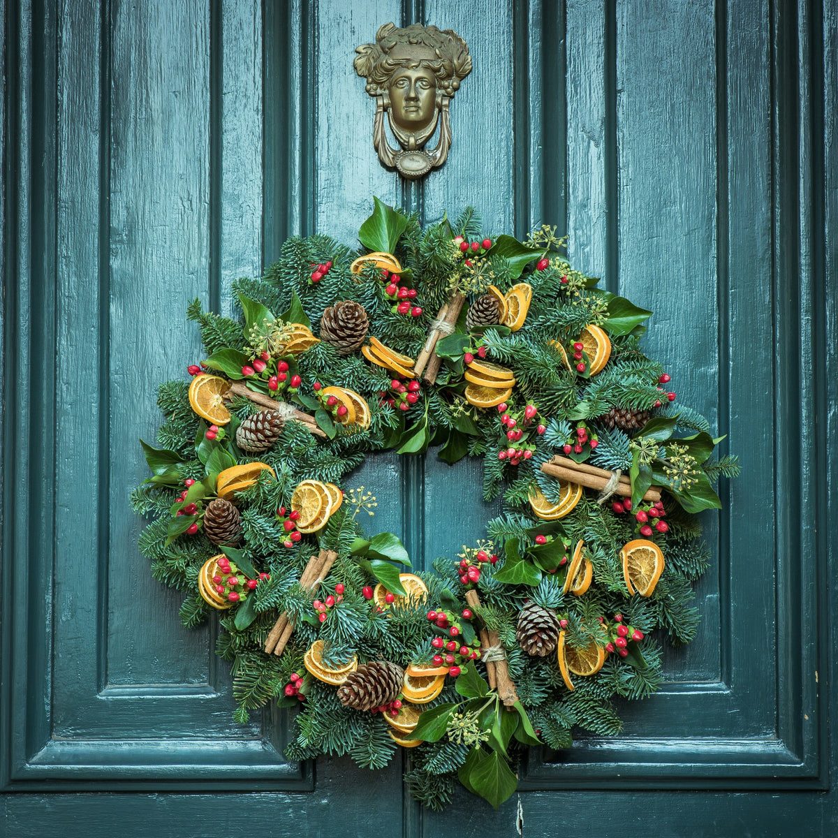 Christmas wreath with dried oranges, cinnamon and berries on a teal front door