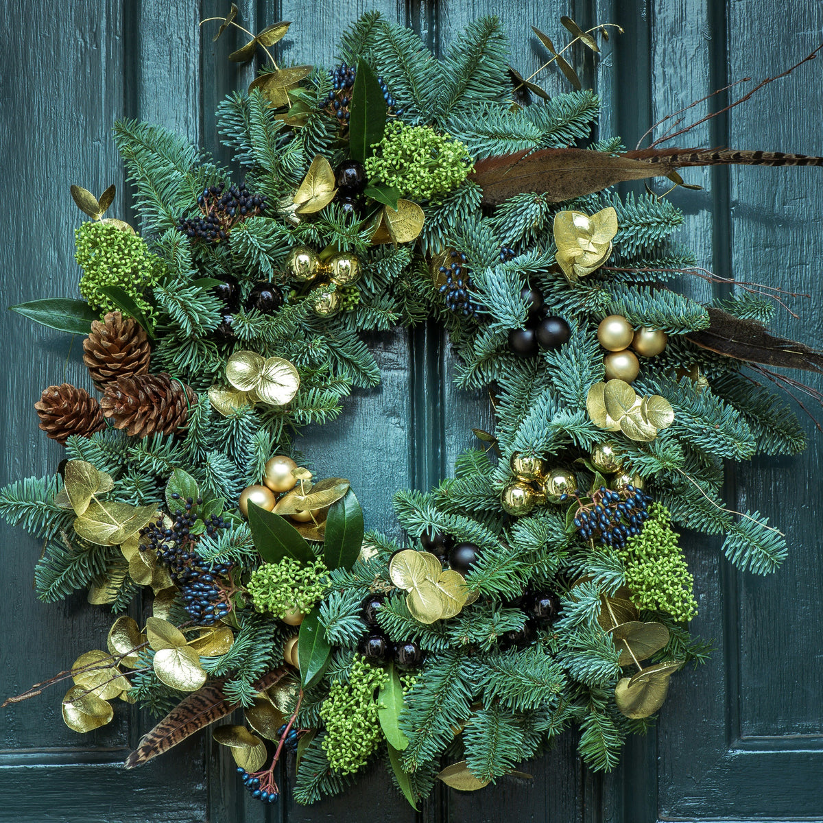 Christmas wreath with gilded leaves, berries and pheasant feathers on a teal door