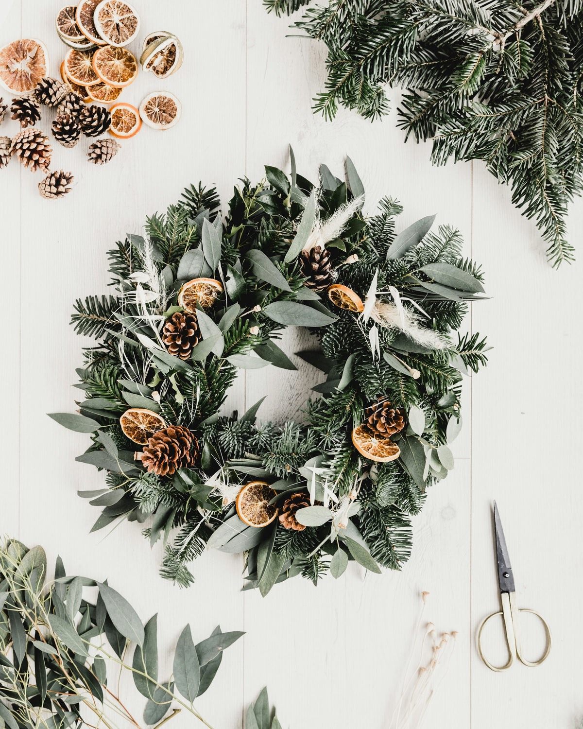 Fresh wreath with dried orange slices and pine cones, with scissors and foliage on a table